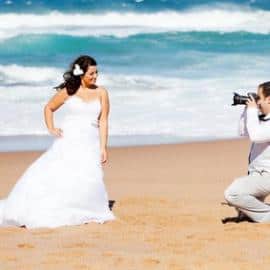 groom taking bride's photos on beach